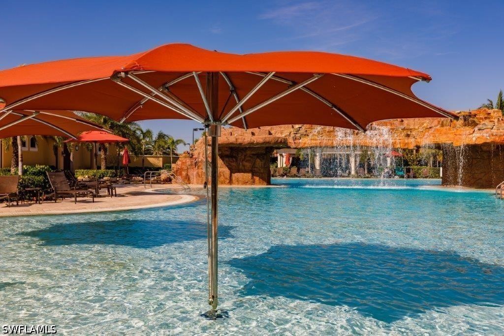 Swimming pool with a large orange umbrella and rock waterfall.