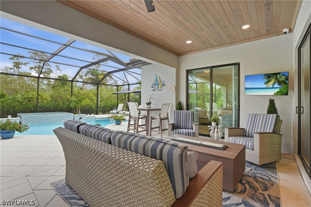 Covered lanai with wicker seating beside a screened swimming pool, with a wood-plank ceiling.