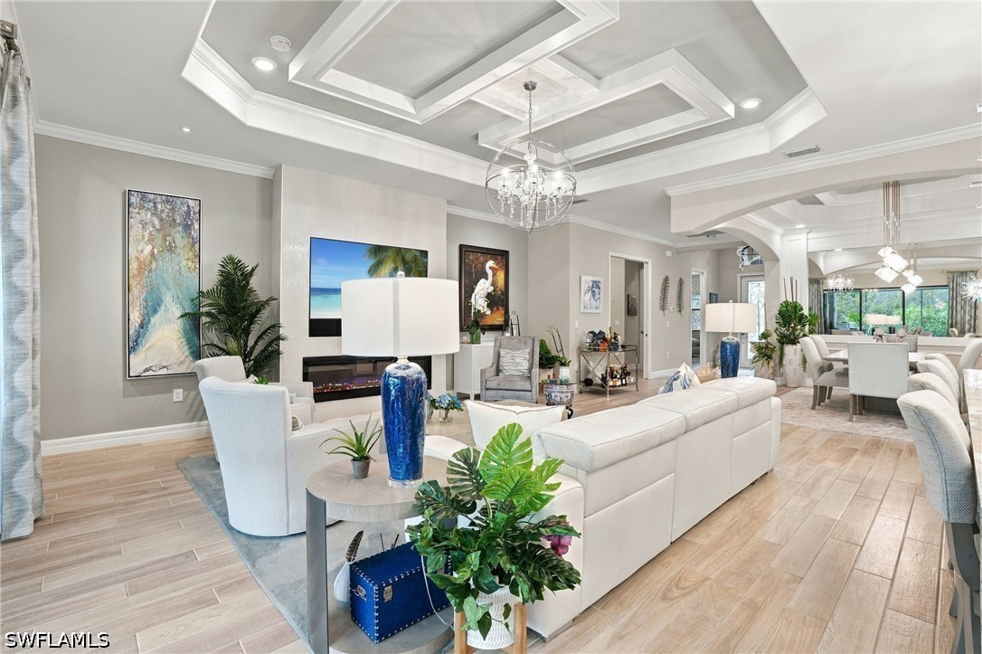 Living room with a white sectional, fireplace, and coffered ceiling opening to a dining area.
