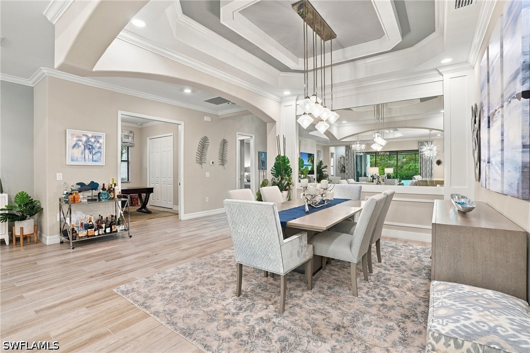 Furnished dining room with a layered tray ceiling, geometric pendant lights, and a mirror reflecting the living area.