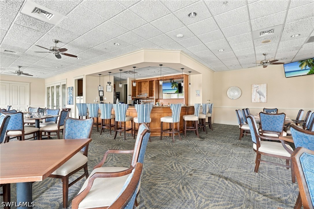 Furnished dining room with a long wooden bar, high stools, and blue-upholstered chairs.