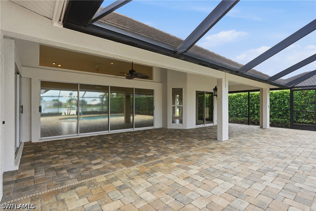 Covered lanai with a paver floor, screened roof, ceiling fan, and wide sliding glass doors.