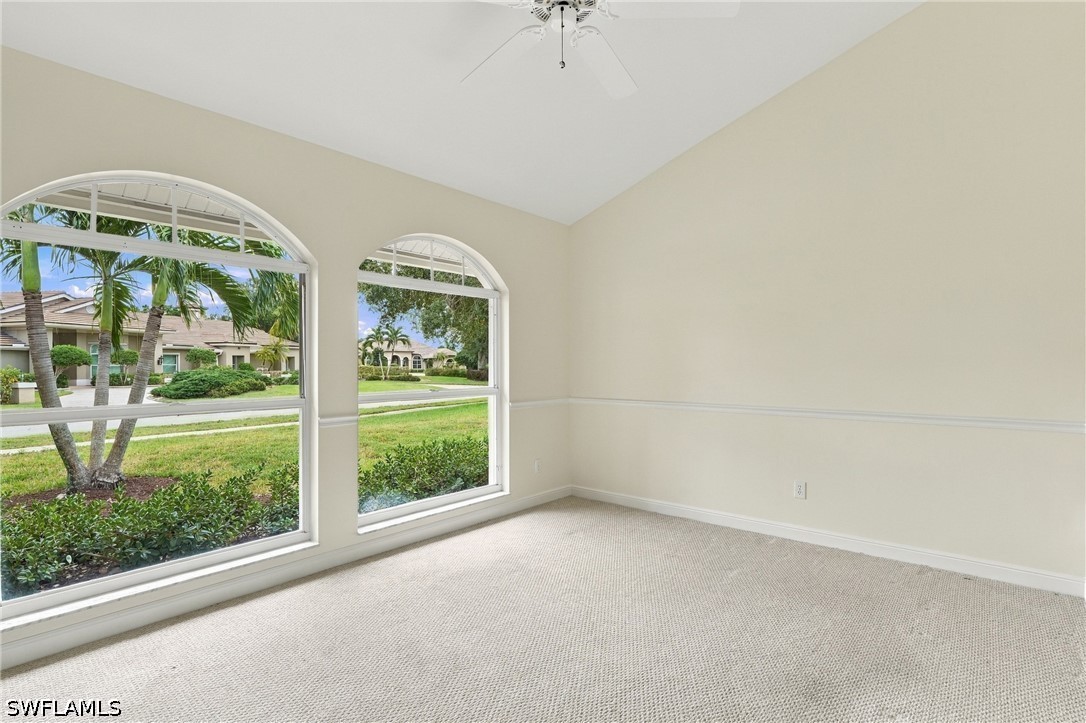 Empty carpeted room with a vaulted ceiling, ceiling fan, and large arched windows overlooking the street.
