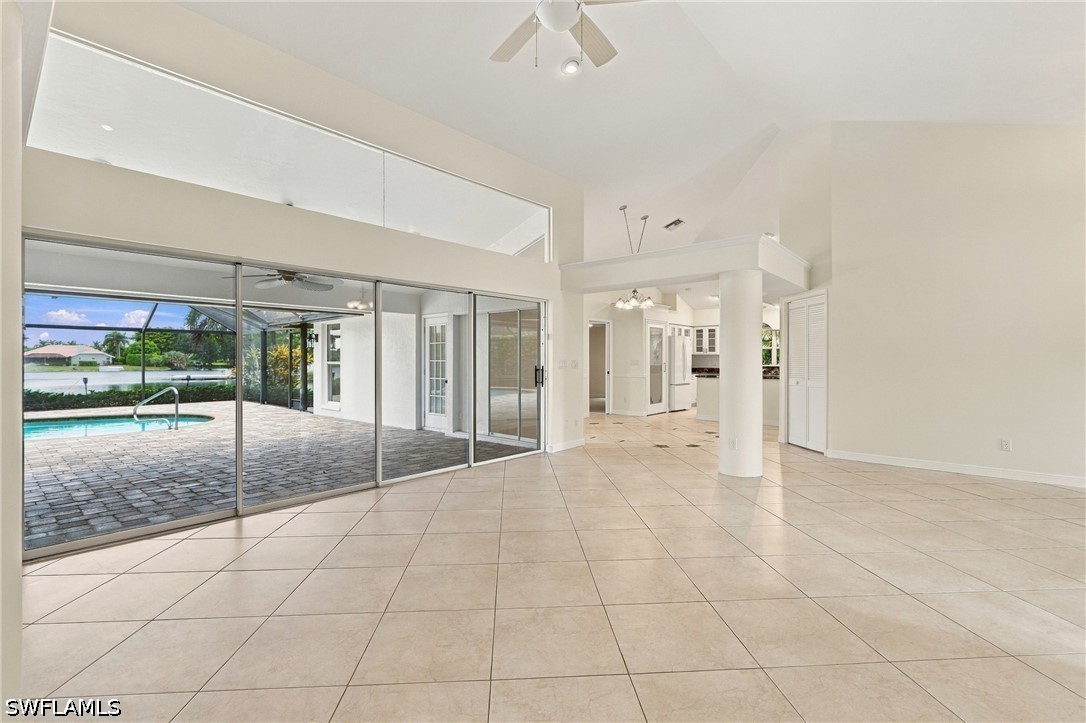 Vacant living room with vaulted ceiling, tile floors, and sliding doors overlooking a pool.