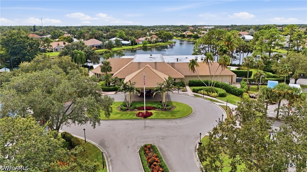Aerial view of a tiled-roof building beside a lake, with a circular driveway and landscaped entrance.
