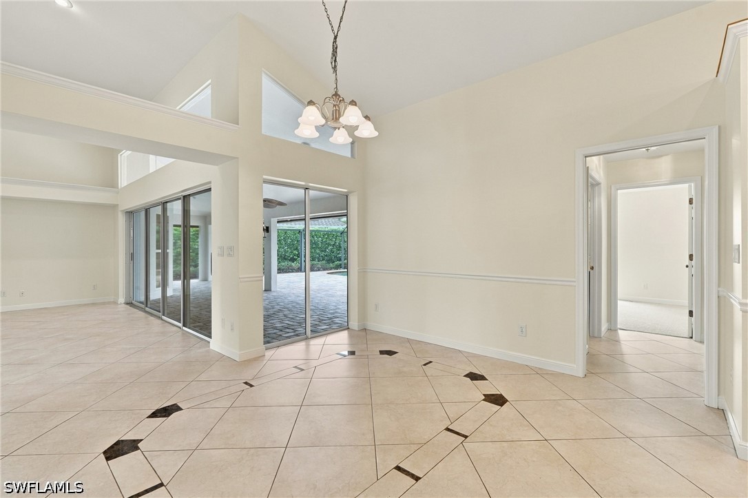 Vacant tiled living area with a high ceiling, chandelier, and sliding glass doors to a patio.