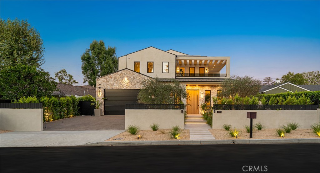 Modern two-story home with stone facade, illuminated entry, balcony, and landscaped front courtyard.