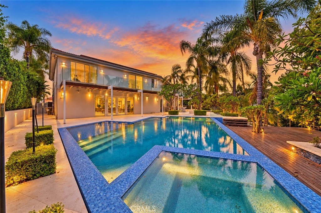 Modern two-story home and angular swimming pool at sunset, surrounded by palm trees.