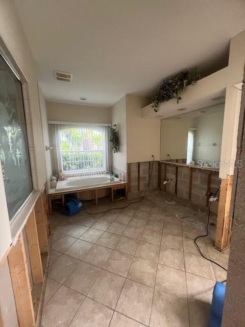 Bathroom under construction with a tiled floor, bathtub beneath a wide window, and exposed wiring.