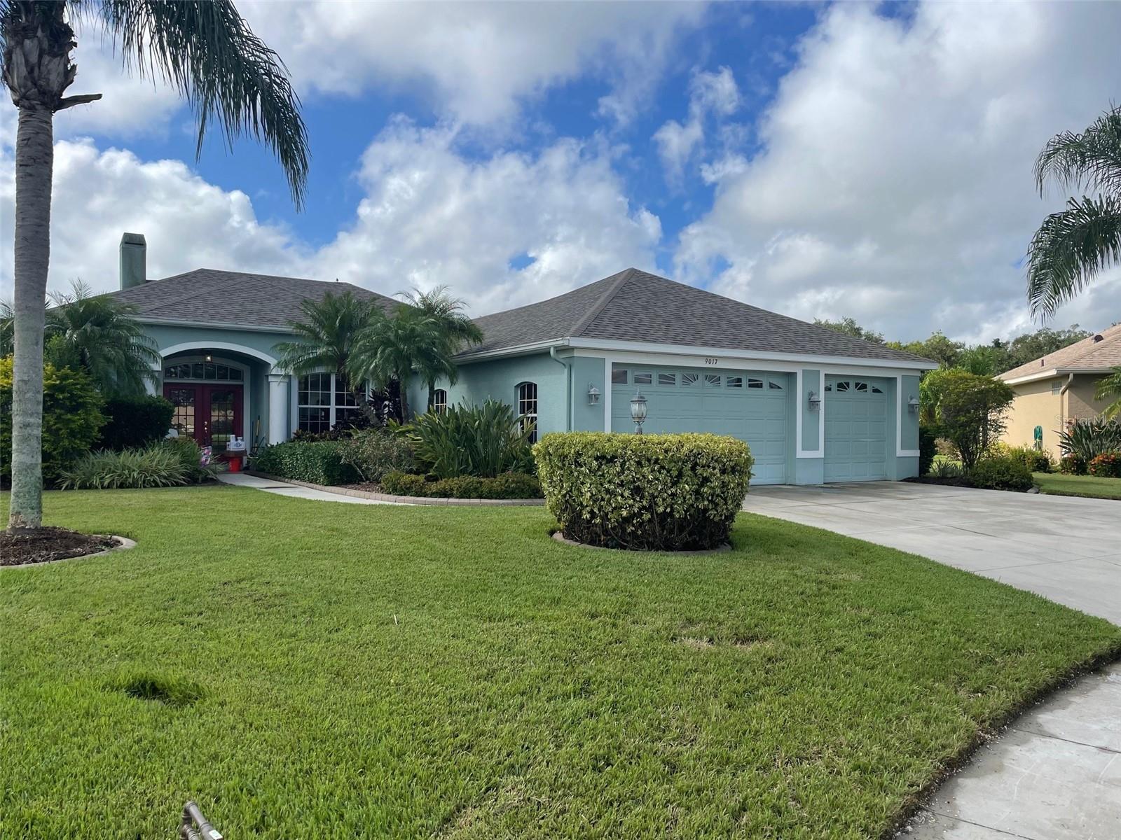 Light blue single-story home with a two-car garage, arched entry, and palm trees.