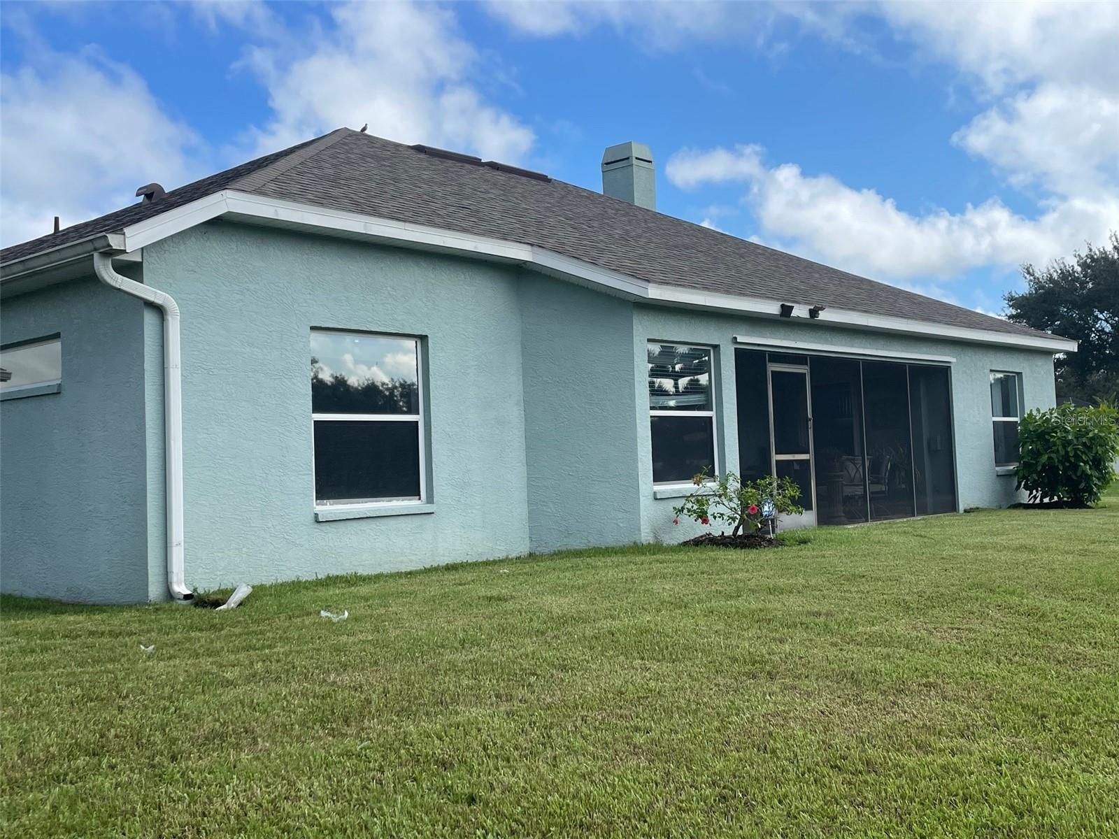 Rear of a light blue stucco house with a screened lanai and broad lawn.