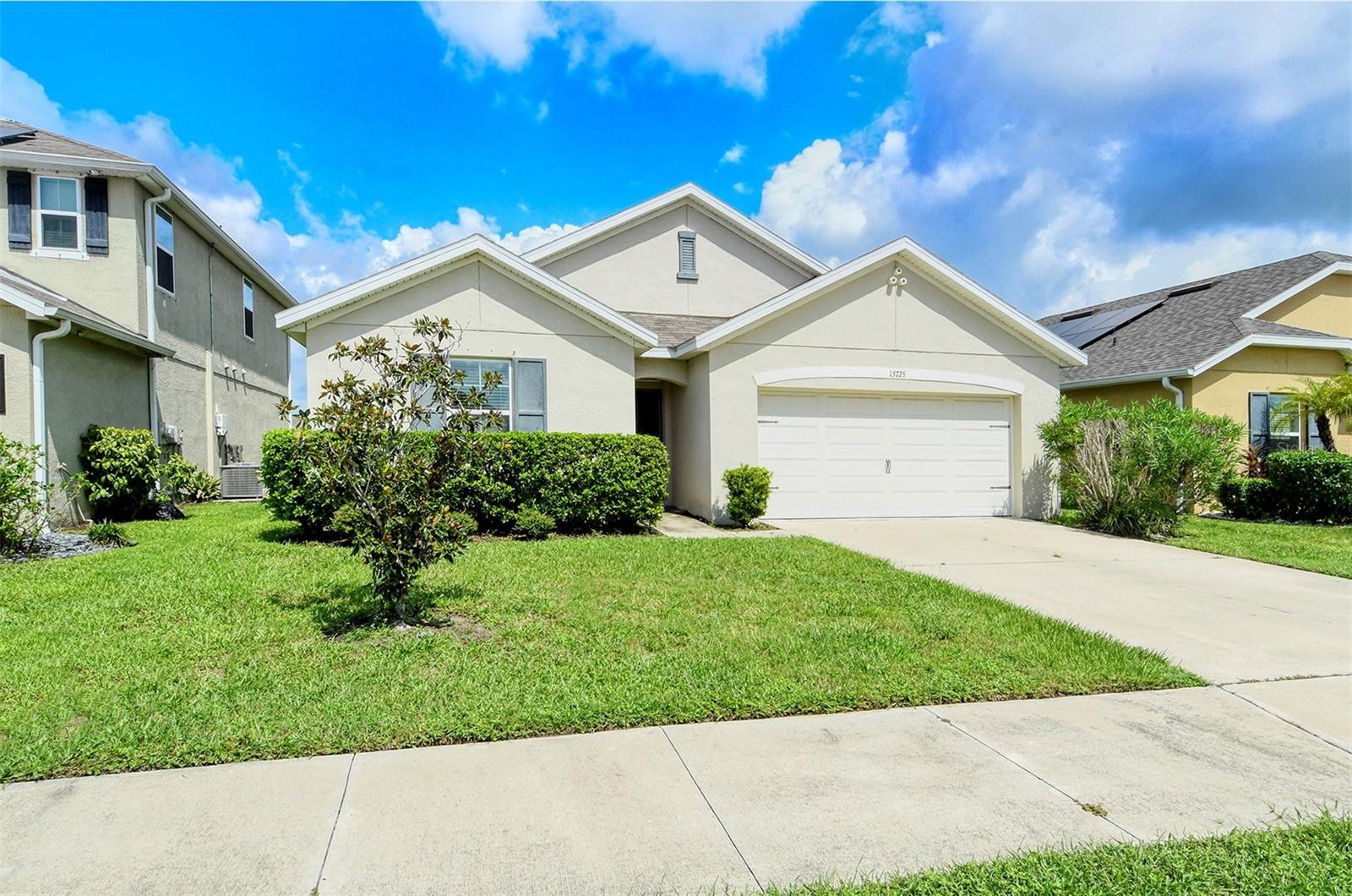 Light stucco home with a two-car garage, concrete driveway, and landscaped front lawn.