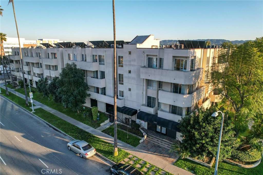 White multi-story apartment building with balconies and black awnings, viewed from above the street.