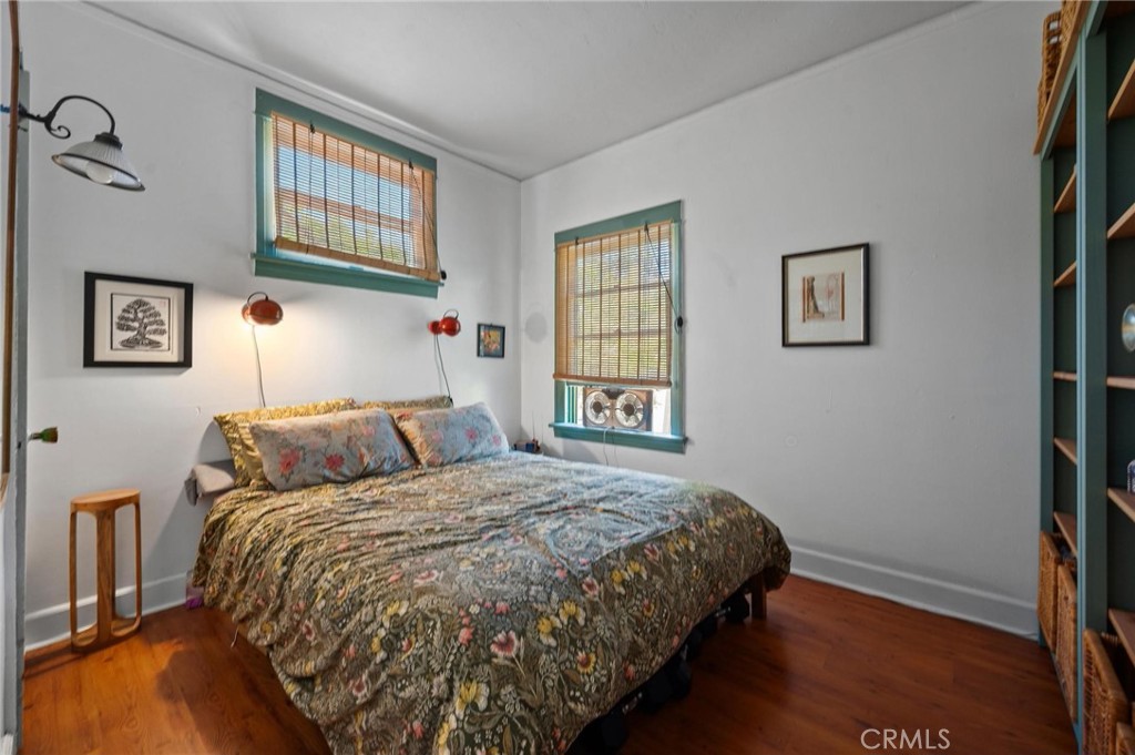 Bedroom with a floral bedspread, green-trimmed windows, and hardwood floors.