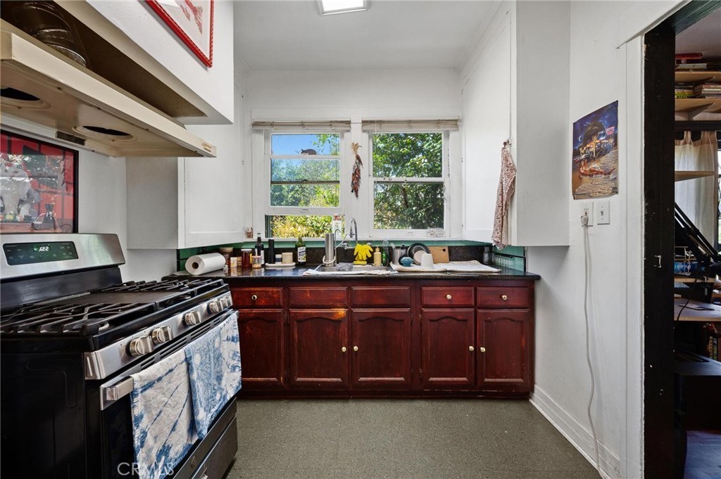 Kitchen with dark wood lower cabinets, a gas range, and a sink beneath two windows.