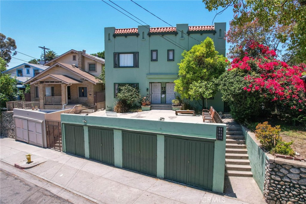 Green stucco apartment building with terracotta roof tiles, front steps, and a row of garages.