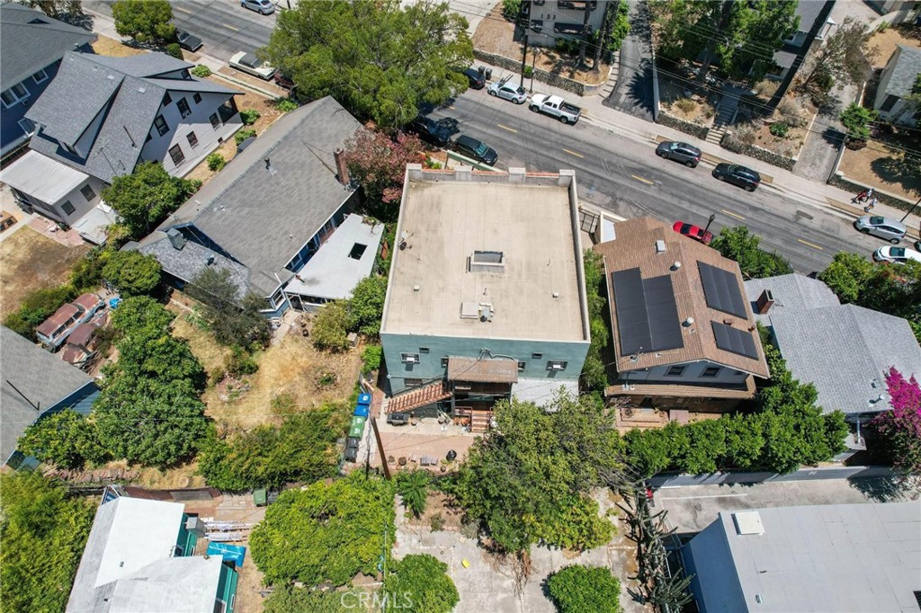 Aerial view of a flat-roofed home among leafy residential properties beside a street.