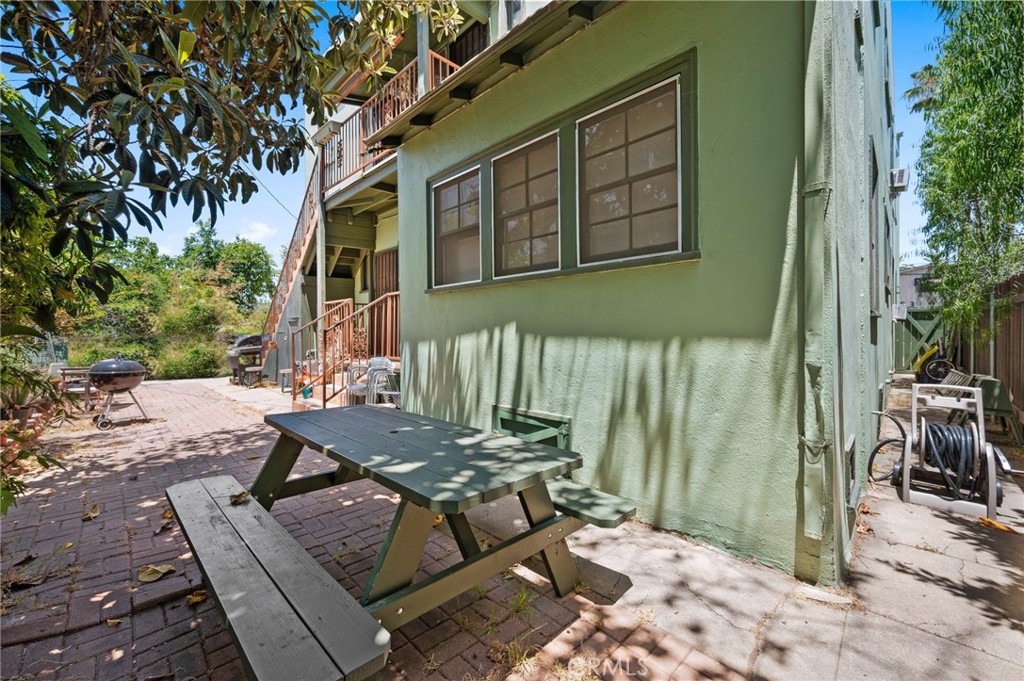 Shaded courtyard beside a green apartment building, with a picnic table, brick paving, and barbecue grill.