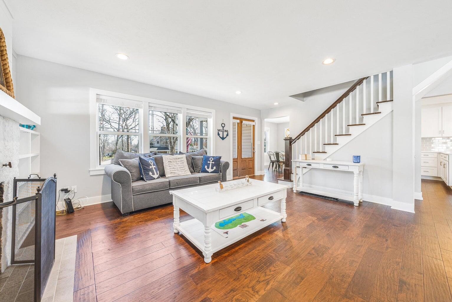 Bright living room with gray sofa, white coffee table, hardwood floors, and staircase.