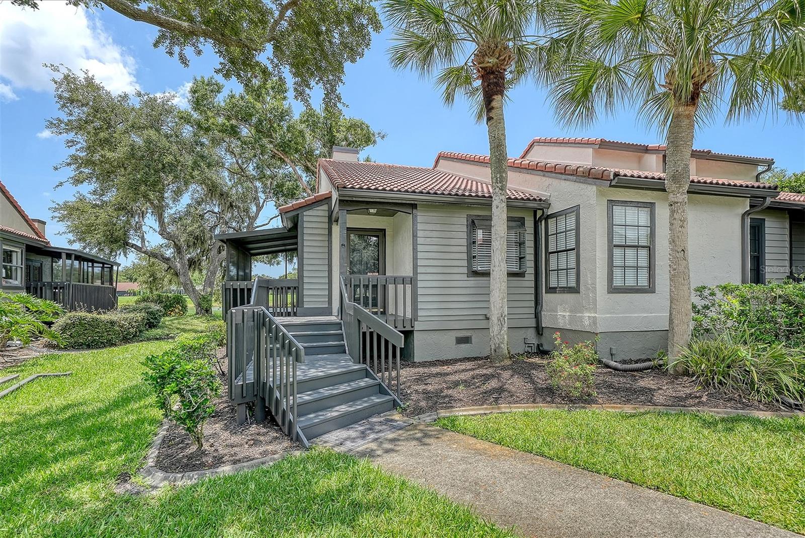 Light-colored home with red tile roof, gray entry stairs, and palm trees.