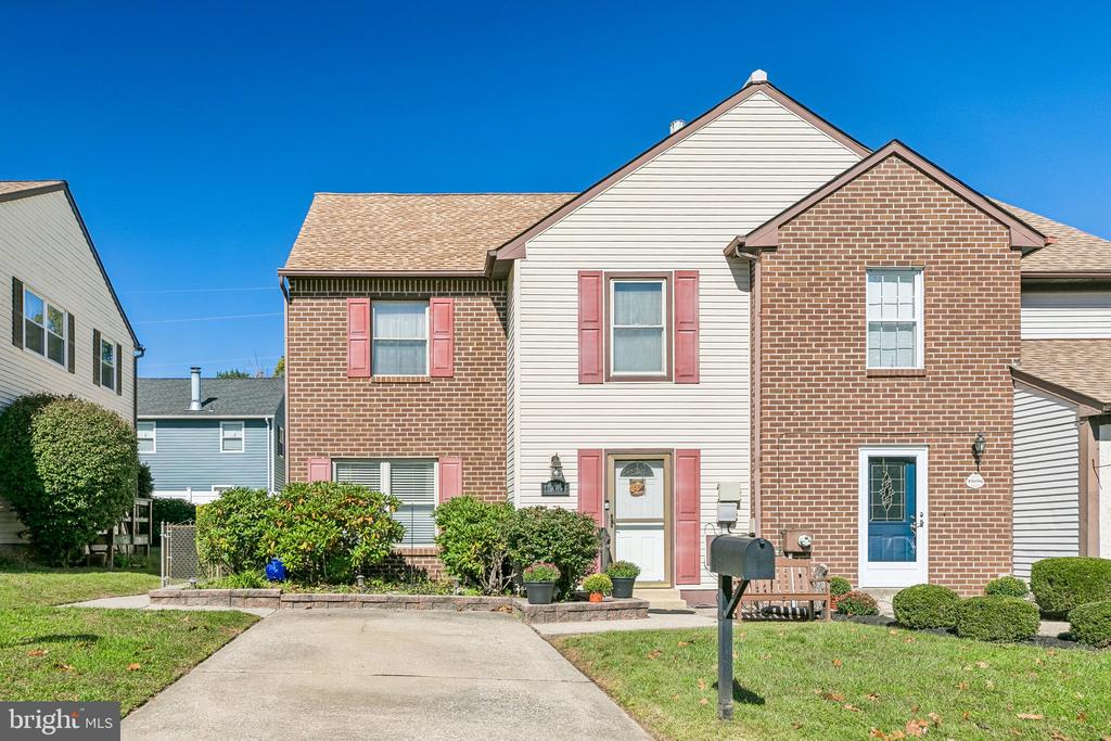 Attached townhouse with brick and light siding, pink shutters, landscaped beds, and a concrete driveway.