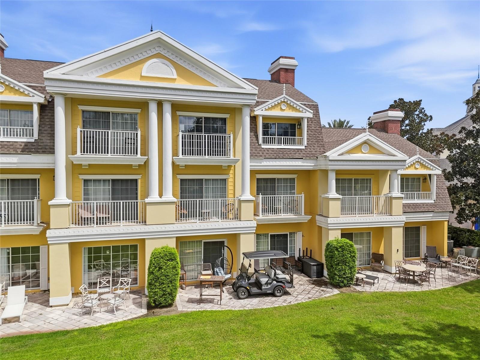 Yellow multi-story residence with white columns, balconies, furnished patios, and a golf cart on the lawn.