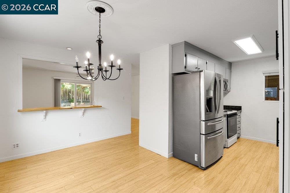 Unfurnished kitchen with gray cabinets, stainless steel appliances, light wood floors, and a pass-through dining counter.