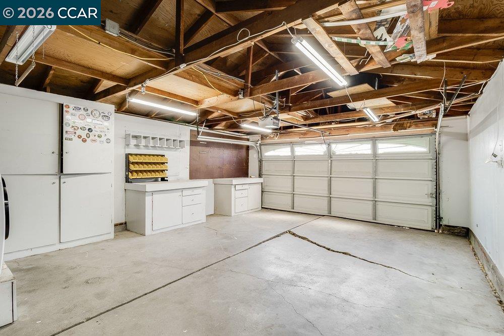 Garage with exposed wooden rafters, white workbenches and cabinets, and a closed sectional door.