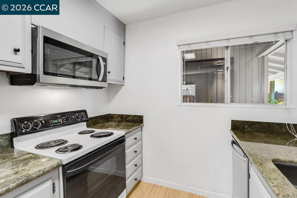 Kitchen with white cabinets, an electric range, and a wide window above the sink.