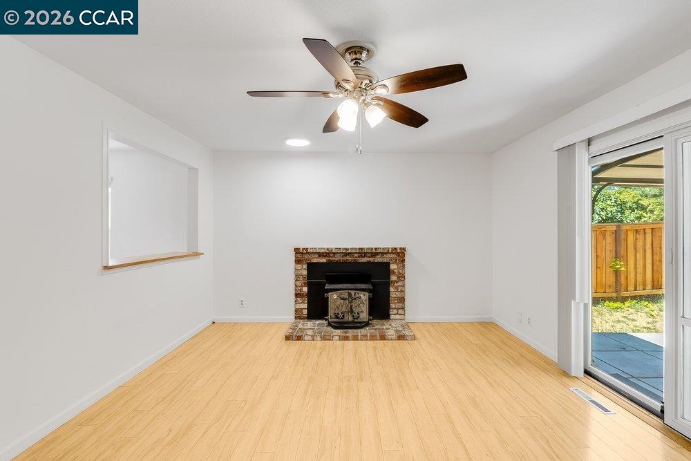 Vacant living room with brick fireplace, ceiling fan, and sliding glass door to patio.