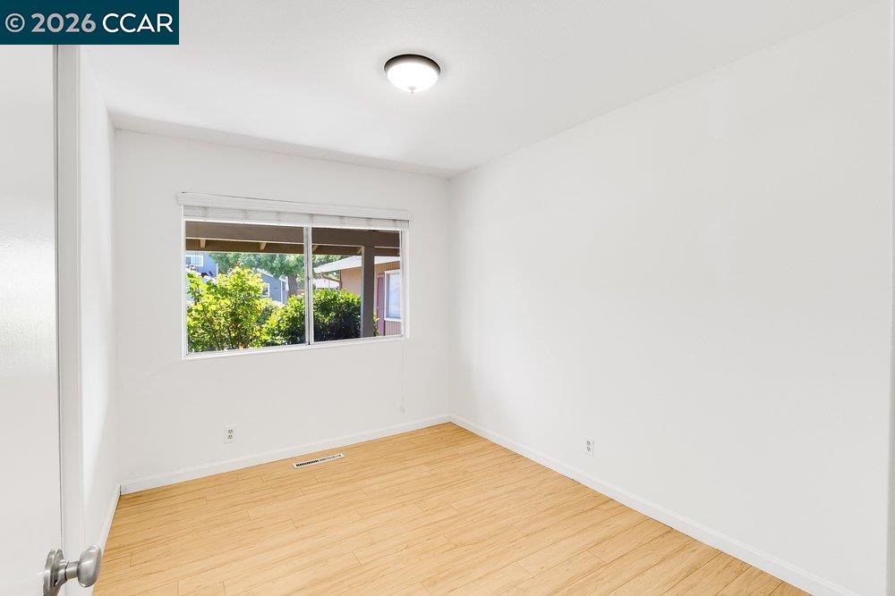 Empty room with light wood flooring, a wide window, and a flush-mount ceiling light.