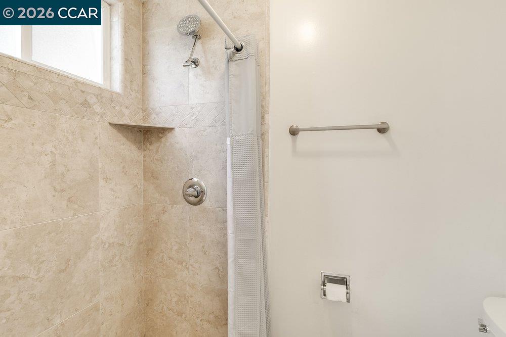 Tiled bathroom shower with a handheld showerhead, corner shelf, and window.