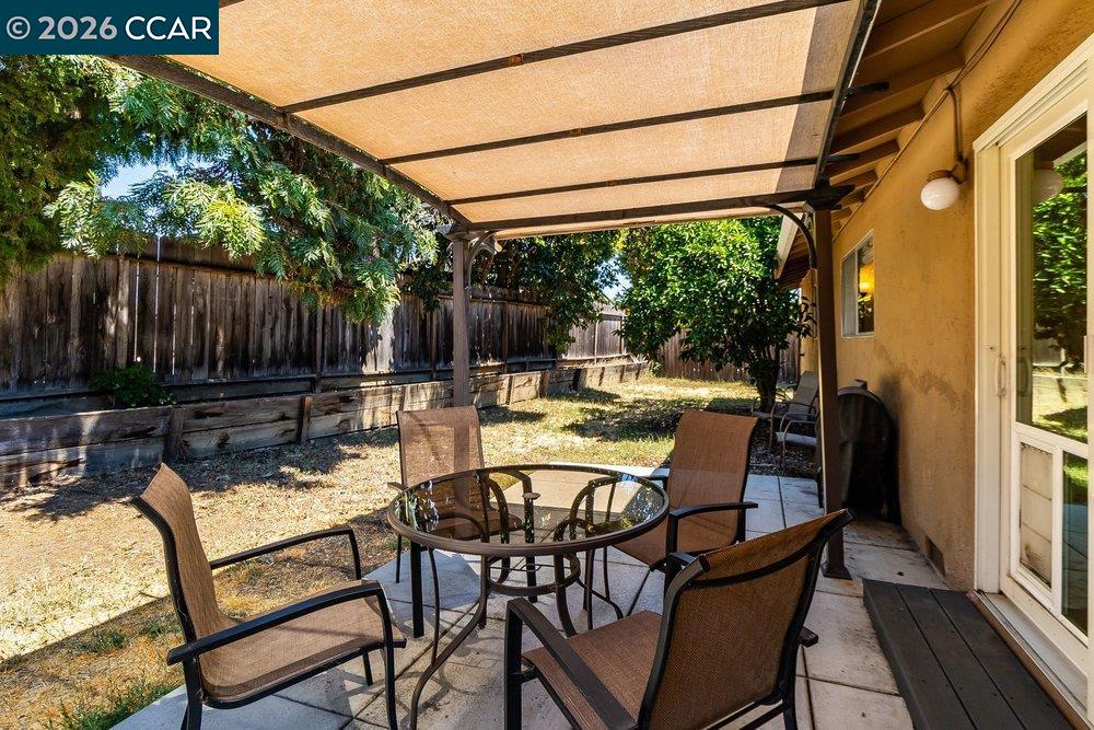 Covered backyard patio with a glass-top dining table and chairs beside a fenced yard.