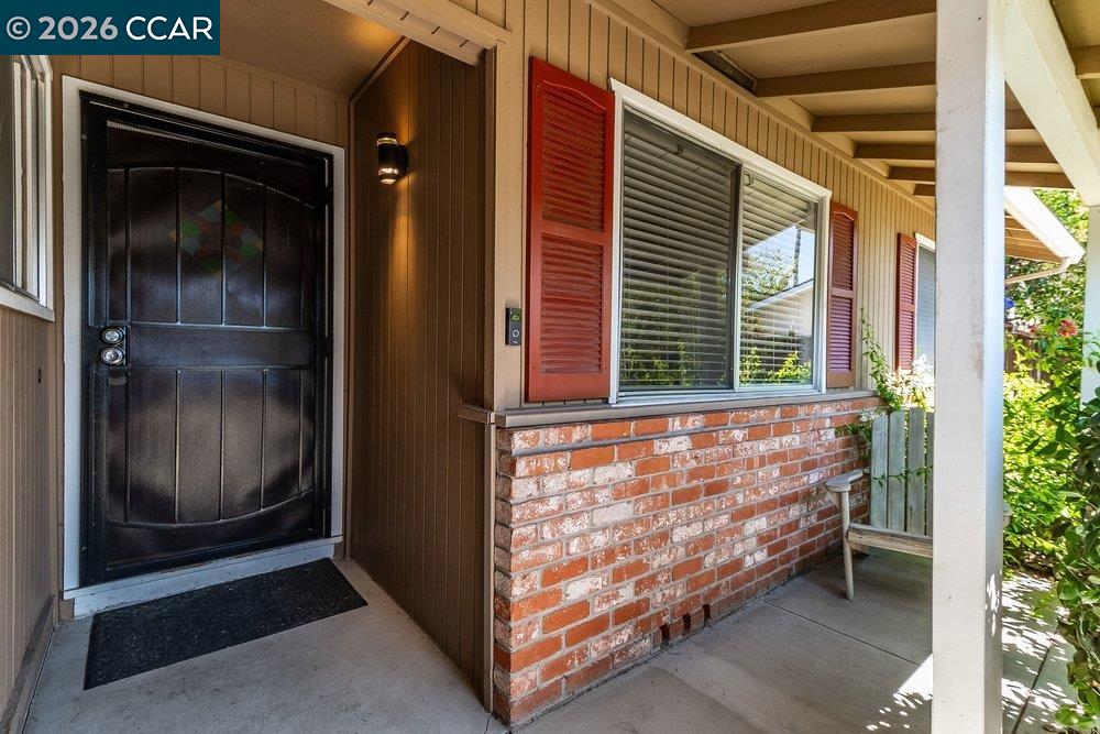Covered front porch with a black door, red shutters, and brick facade.