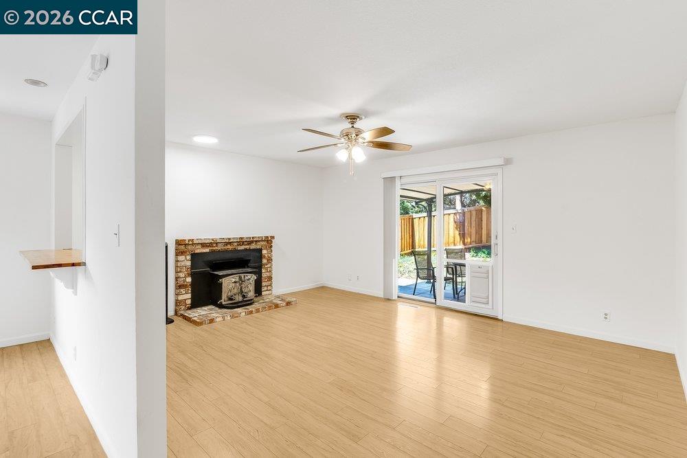 Empty living room with a brick fireplace, ceiling fan, and sliding glass doors to a patio.