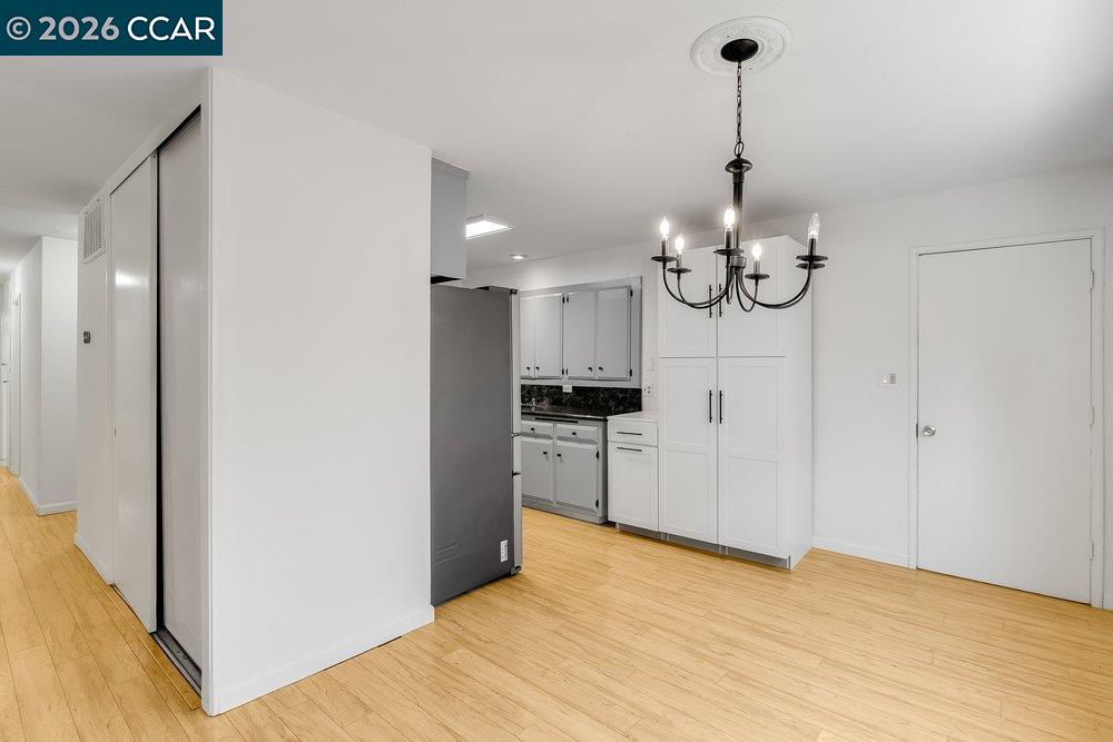 Kitchen with white cabinets, stainless-steel refrigerator, dark countertops, and light wood flooring.