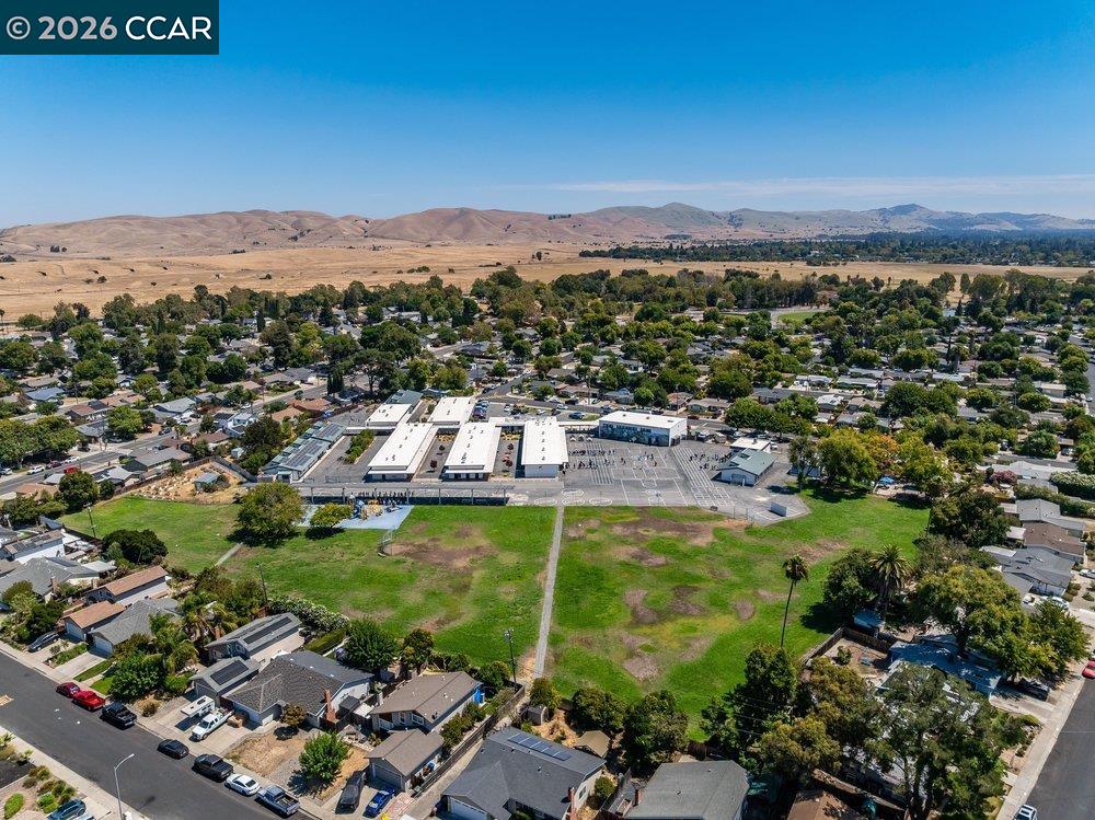 Aerial view of a residential neighborhood, campus buildings, open fields, and distant rolling hills.