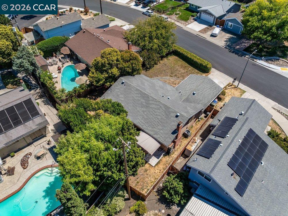 Aerial view of a gray-roofed house with a fenced backyard among neighboring homes.