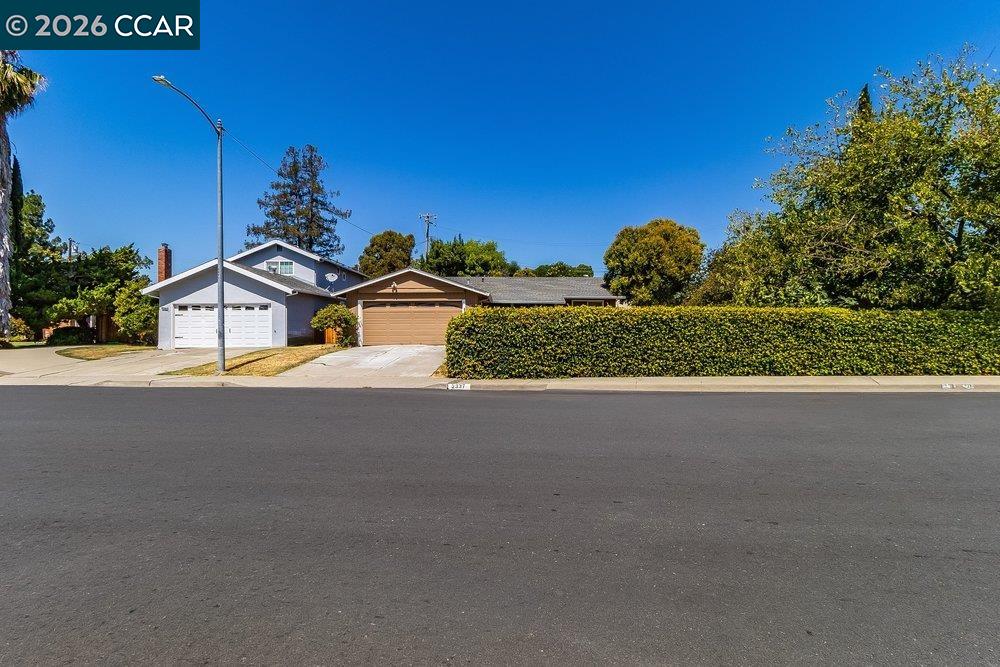 Single-story home with two garages, a long front hedge, and a driveway.