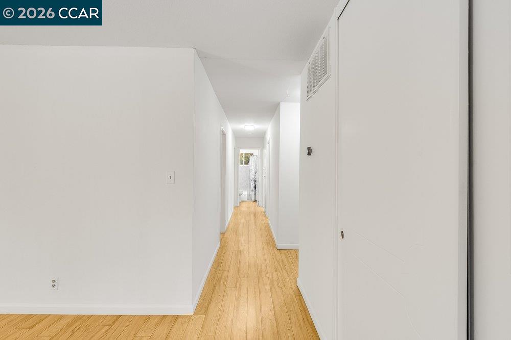 White hallway with light wood flooring and doorways leading toward the back of the home.