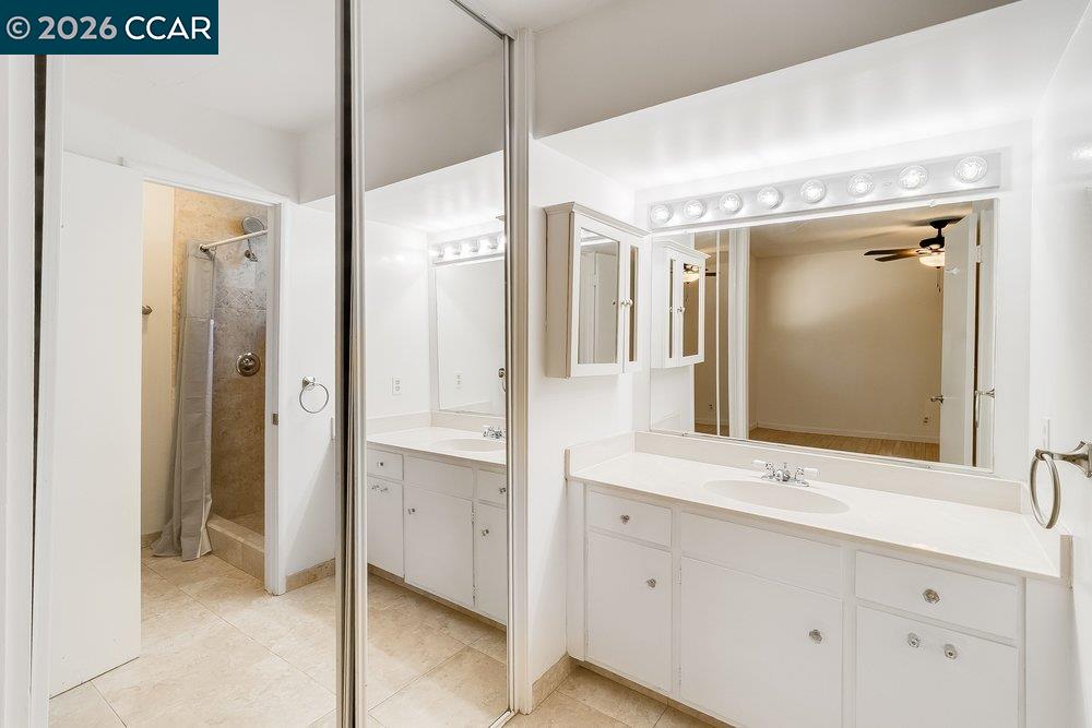 Bathroom with white vanity, large mirrors, and a tiled shower.