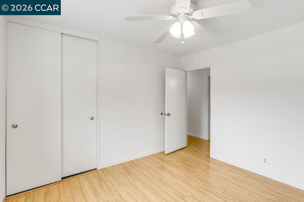 Empty bedroom with sliding closet doors, a ceiling fan, and light wood flooring.