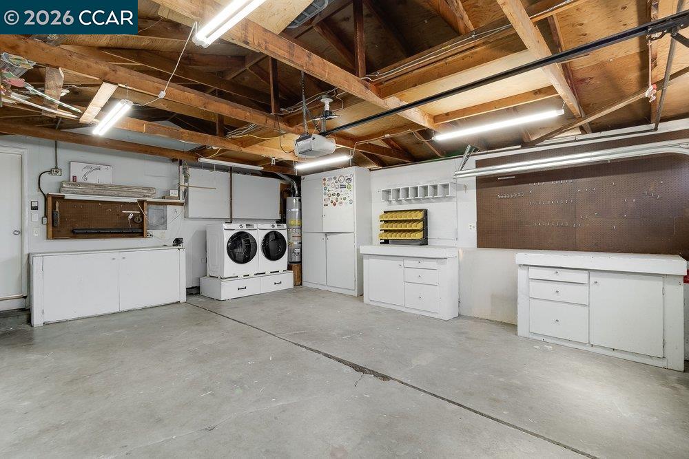 Garage workshop with exposed rafters, washer and dryer, white cabinets, and wall-mounted pegboards.