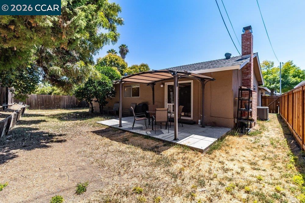 Backyard patio with outdoor seating, brick chimney, mature trees, and fenced yard.