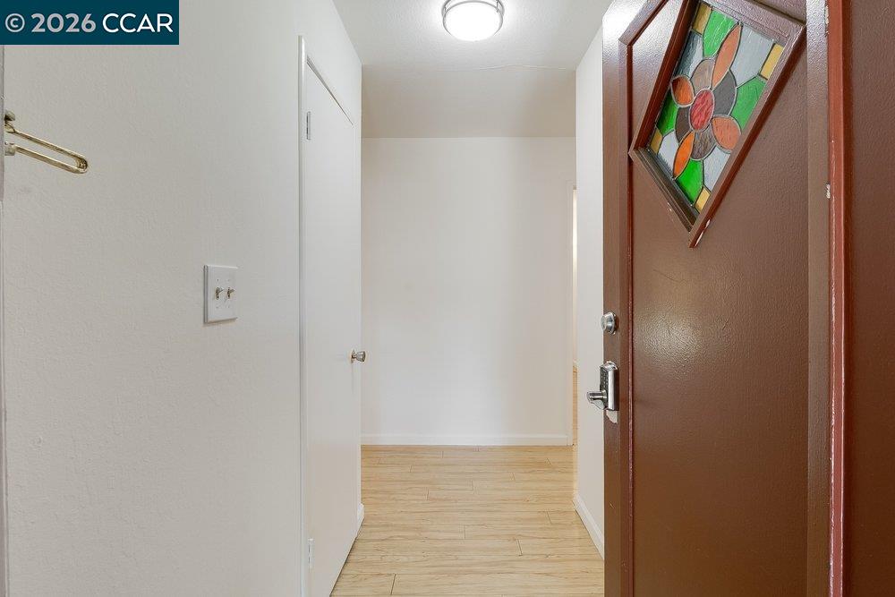 Entryway with light wood-look flooring and an open front door with a colorful stained-glass panel.