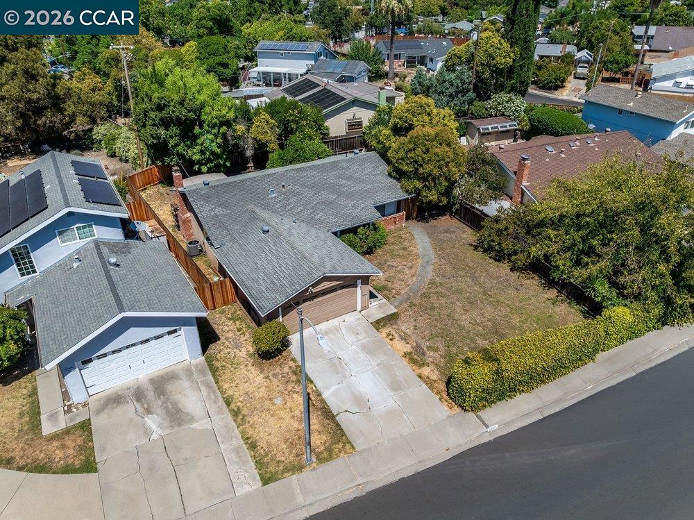 Aerial view of a single-story home with a long driveway, fenced yard, and mature trees.