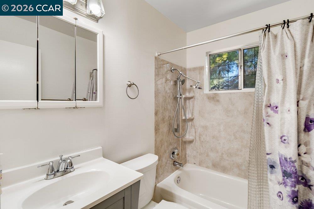 Bathroom with a white vanity, mirrored medicine cabinet, and tiled bathtub beneath a small window.