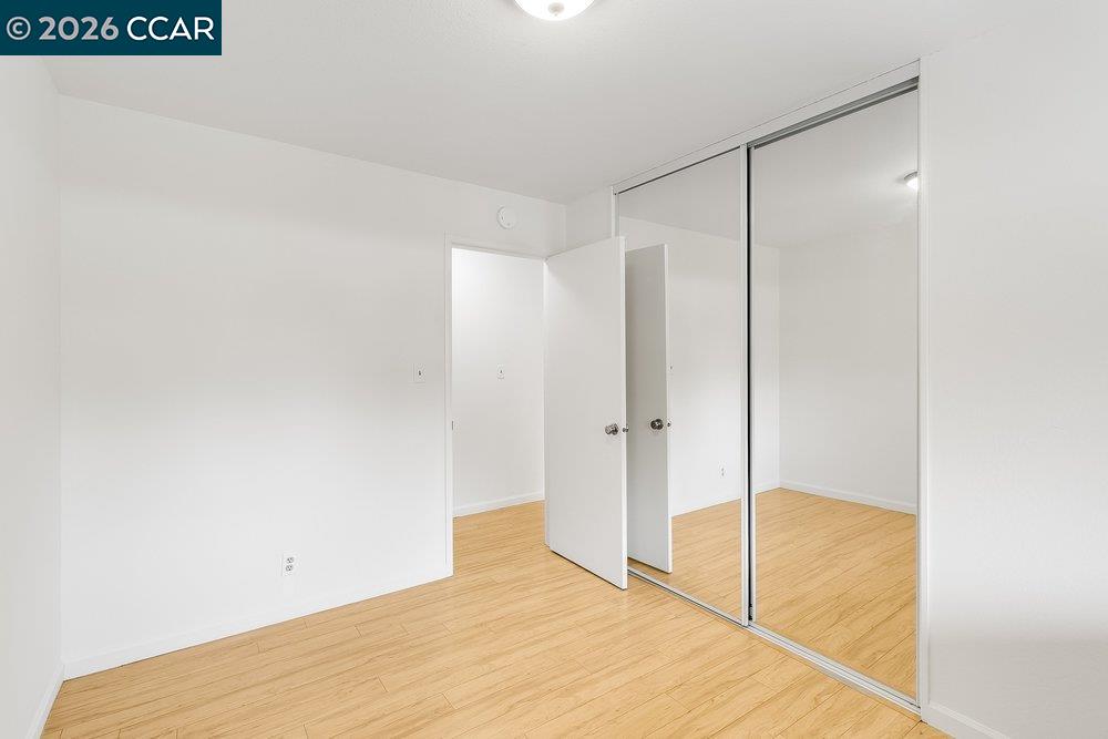 Empty bedroom with light wood-look flooring and mirrored sliding closet doors.