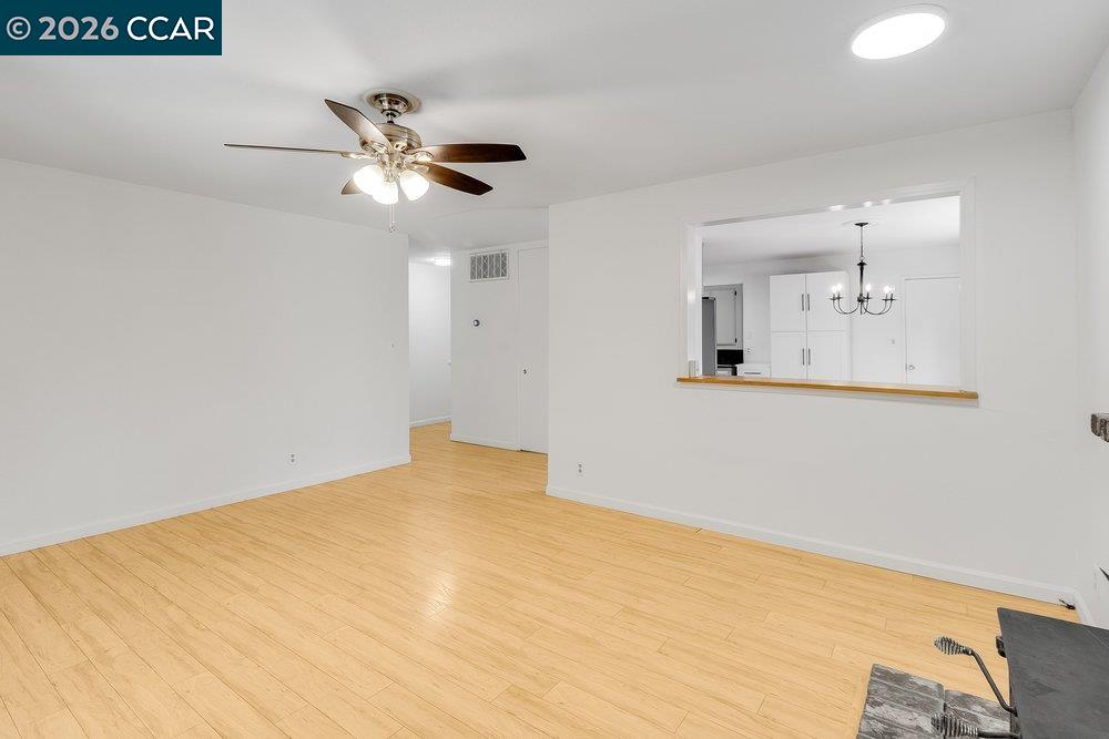 Vacant room with light wood flooring, a ceiling fan, and a pass-through to the kitchen.