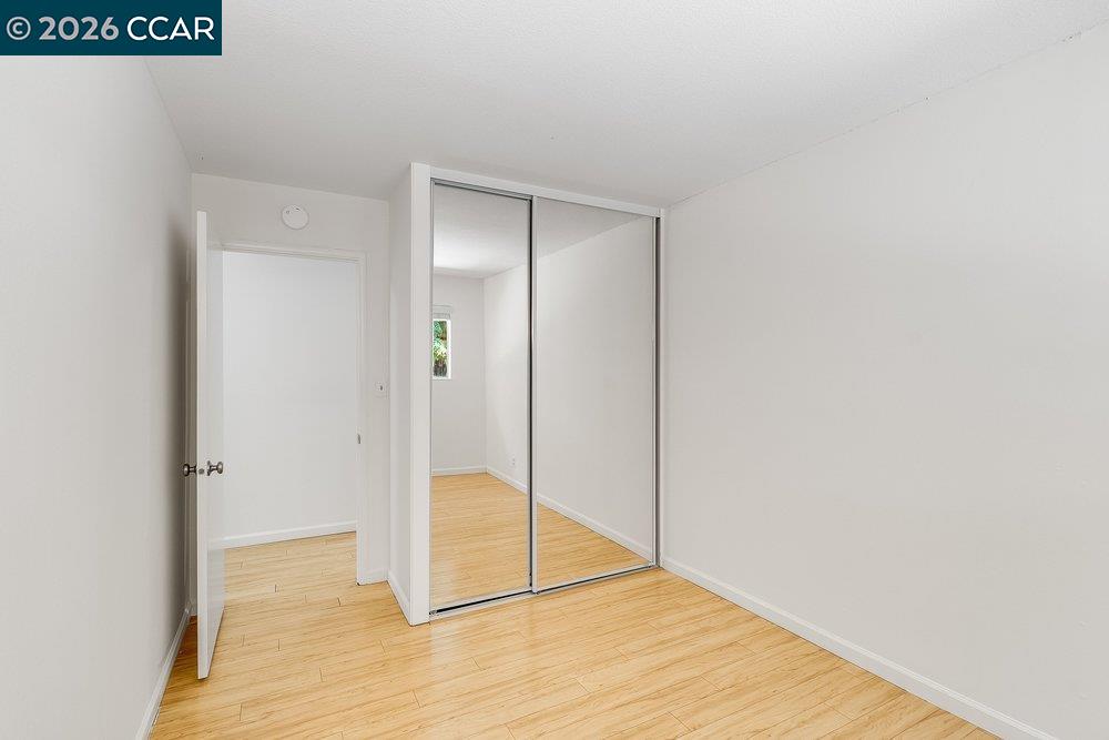 Empty bedroom with light wood flooring and mirrored sliding closet doors.